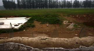 Broken pieces of glass protrude from a wall to keep out trespassers at an illegal golf course which was demolished and turned into a cornfield in the suburbs of Beijing